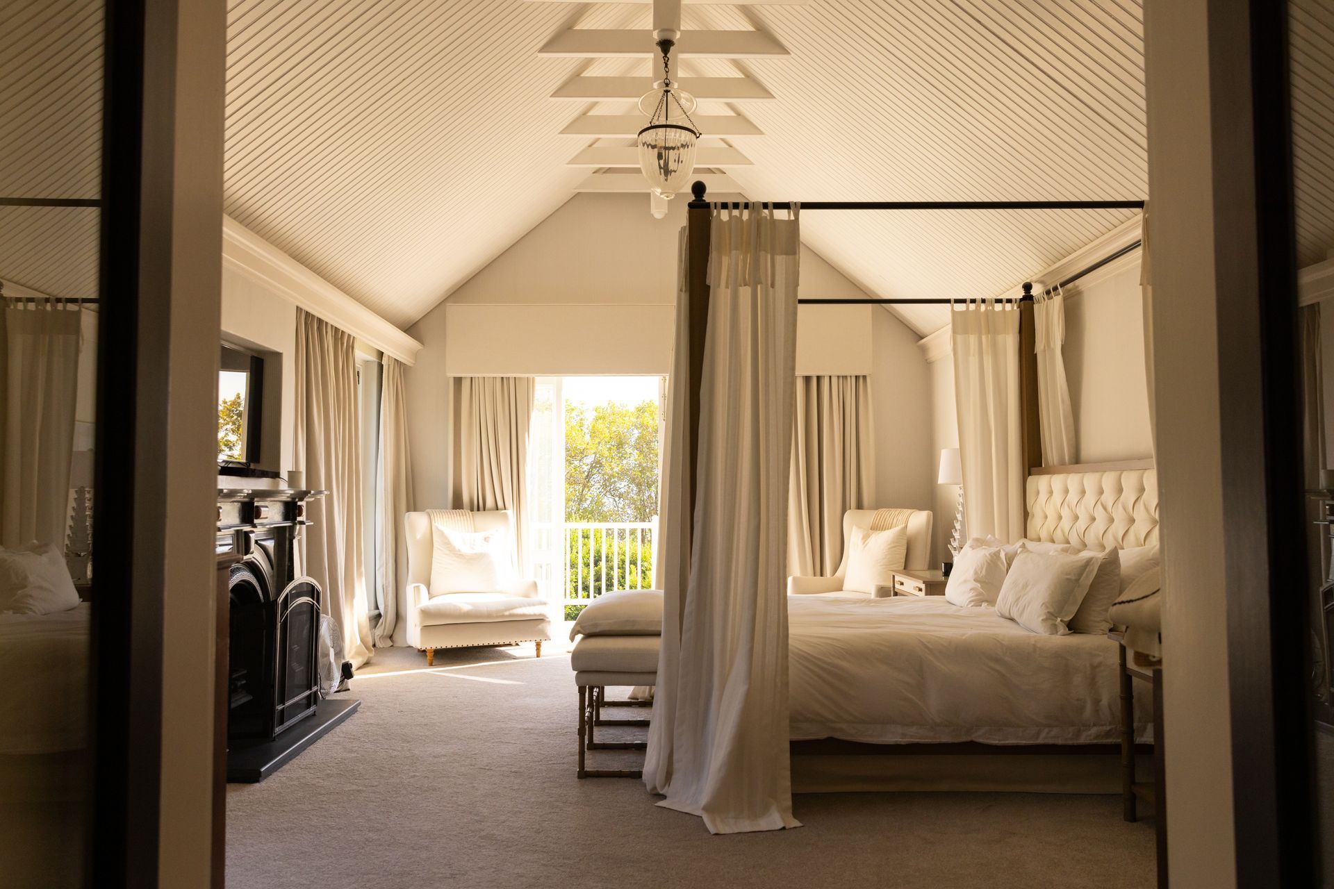 Bedroom with high ceilings and a four-poster bed. Neutral colors, balcony visible, through a doorway.