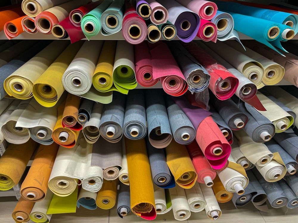 Shelves of colorful fabric rolls in a store; various shades of blue, pink, yellow, and green.