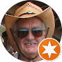 Man in cowboy hat and sunglasses smiles, an orange star badge visible.