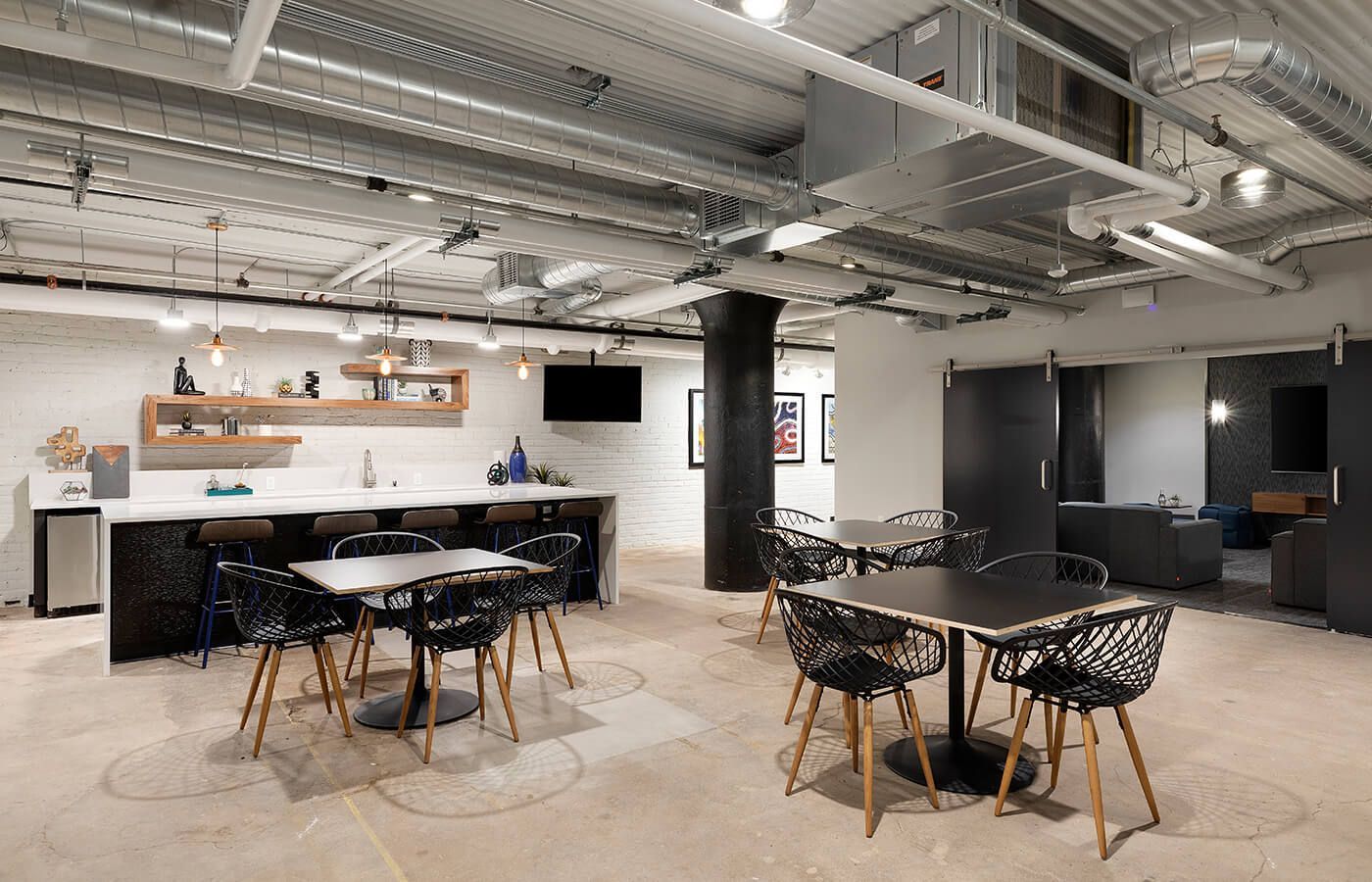 Industrial-style community lounge with a bar, tables, and exposed ductwork.