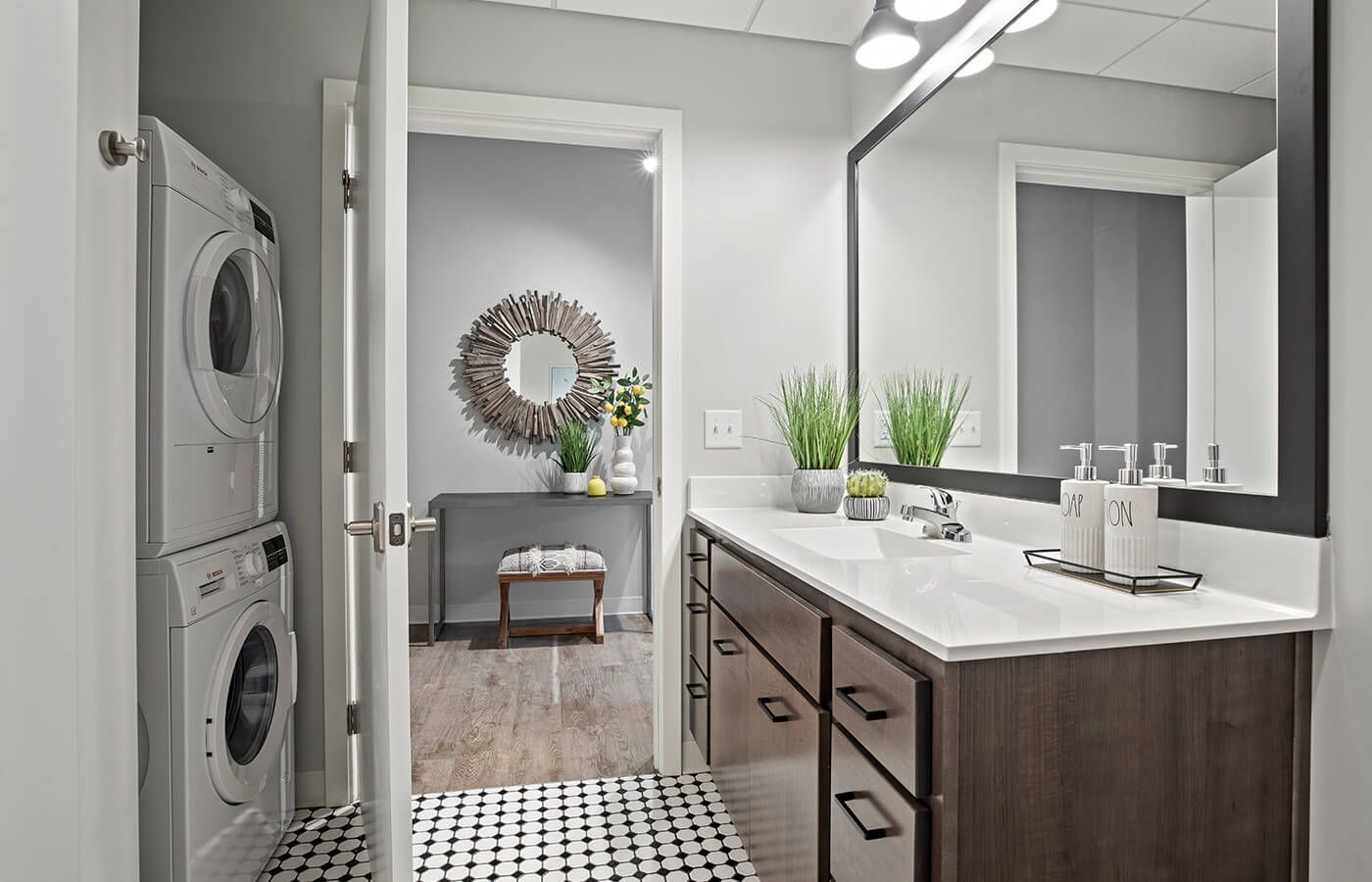 Laundry closet with stacked washer and dryer beside a bathroom vanity and large mirror.