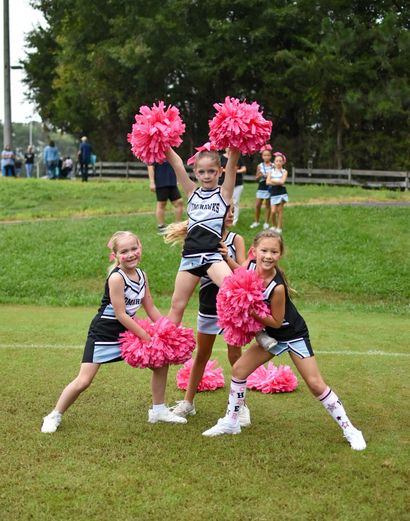 Cheerleader in red uniform performs a backbend on a green and red football field.