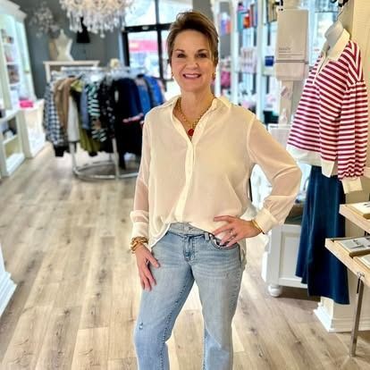 A woman is standing in a clothing store wearing a white shirt and jeans.