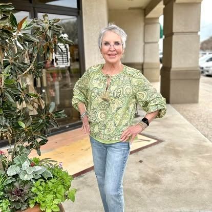 A woman in a green top and jeans is standing in front of a building.