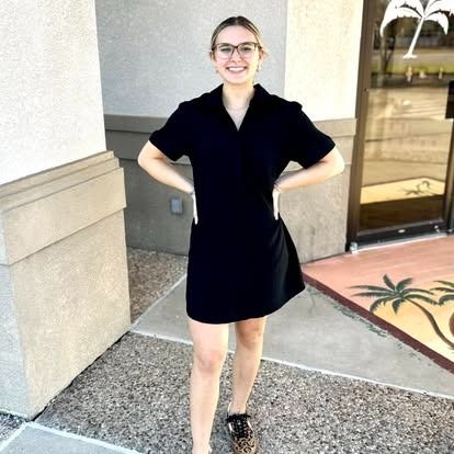 A woman in a black dress and leopard print shoes is standing in front of a building.