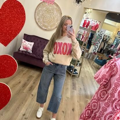 A woman is taking a selfie in a store while wearing a sweater that says xoxo.