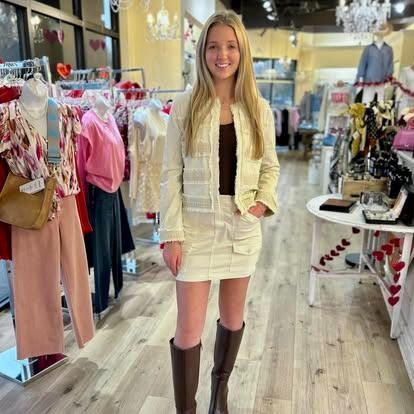 A woman in a white skirt and brown boots is standing in a clothing store.