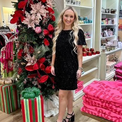 A woman in a black dress is standing in front of a christmas tree in a store.