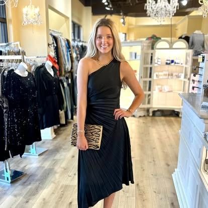 A woman in a black dress is standing in a clothing store.