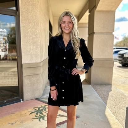 A woman in a black dress is standing in front of a building.