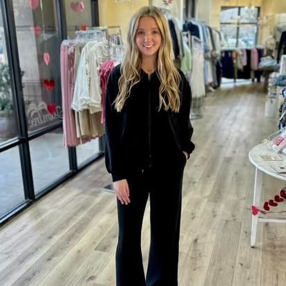 A woman in a black jumpsuit is standing in a clothing store.