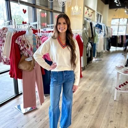 A woman in a white sweater and blue jeans is standing in a clothing store.