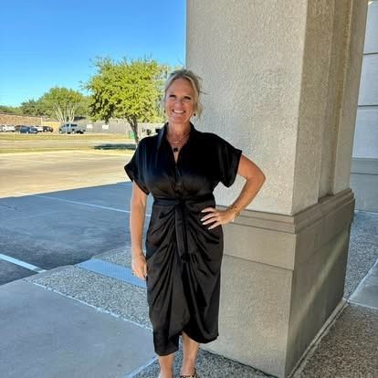 A woman in a black dress is standing in front of a building.