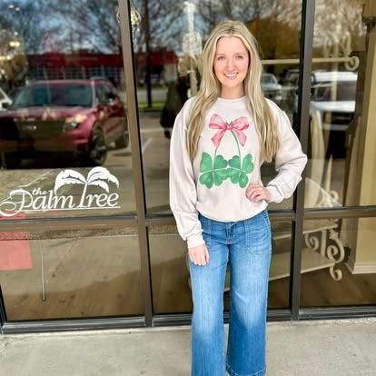 A woman wearing a sweater and jeans is standing in front of a store.