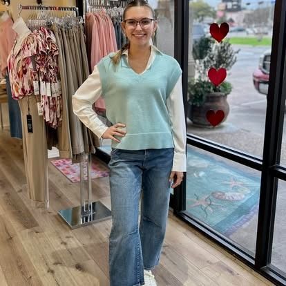 A woman wearing a blue vest and jeans is standing in a clothing store.