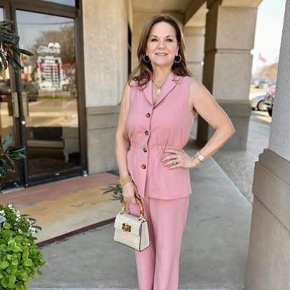 A woman in a pink suit is standing in front of a building.