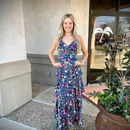 A woman in a floral dress is standing in front of a building.