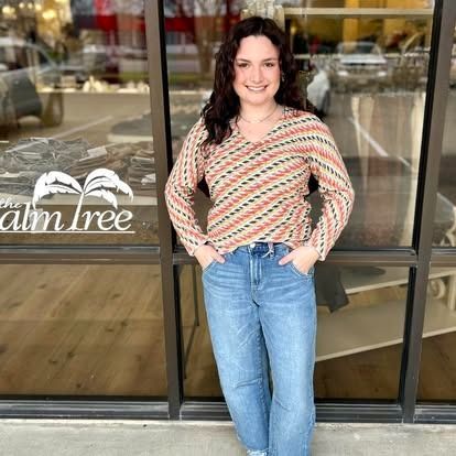 A woman in a striped shirt and jeans is standing in front of a store window.