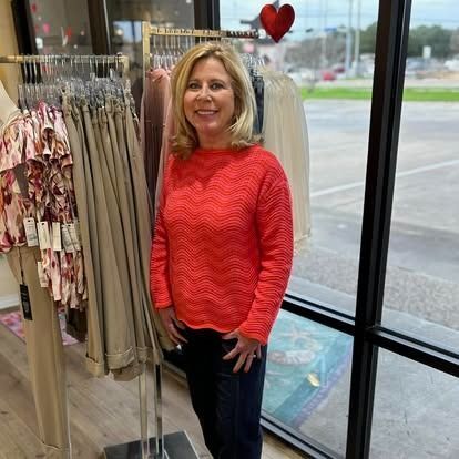 A woman in a red sweater is standing in front of a window in a store.