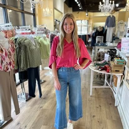 A woman in a pink shirt and blue jeans is standing in a clothing store.