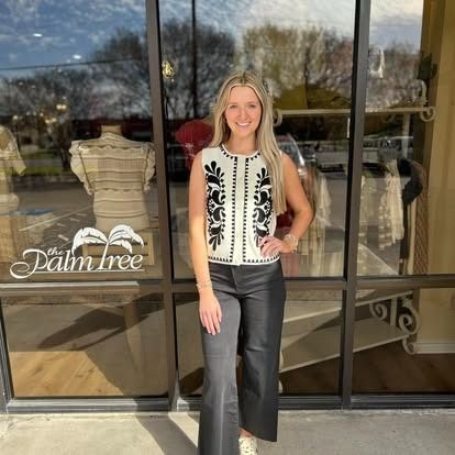 A woman in a white top and black pants is standing in front of a store.