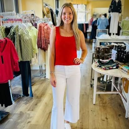 A woman in a red tank top and white pants is standing in a clothing store.