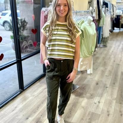 A woman wearing a striped crop top and green pants is standing in a store.