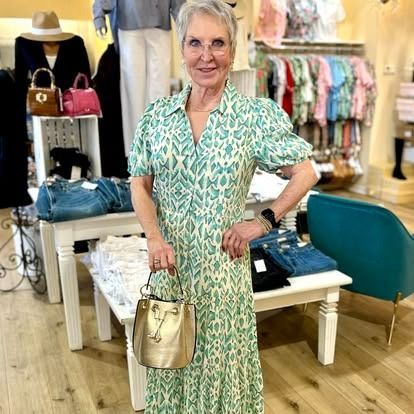 A woman in a green dress is standing in a store holding a purse.
