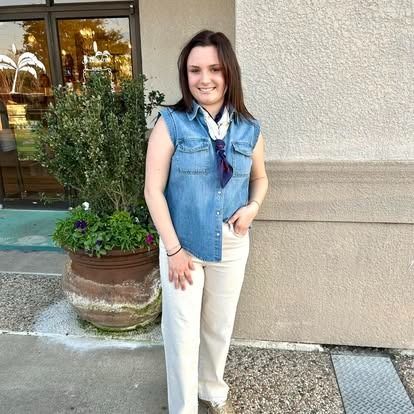 A woman wearing a denim vest and white pants is standing in front of a building.