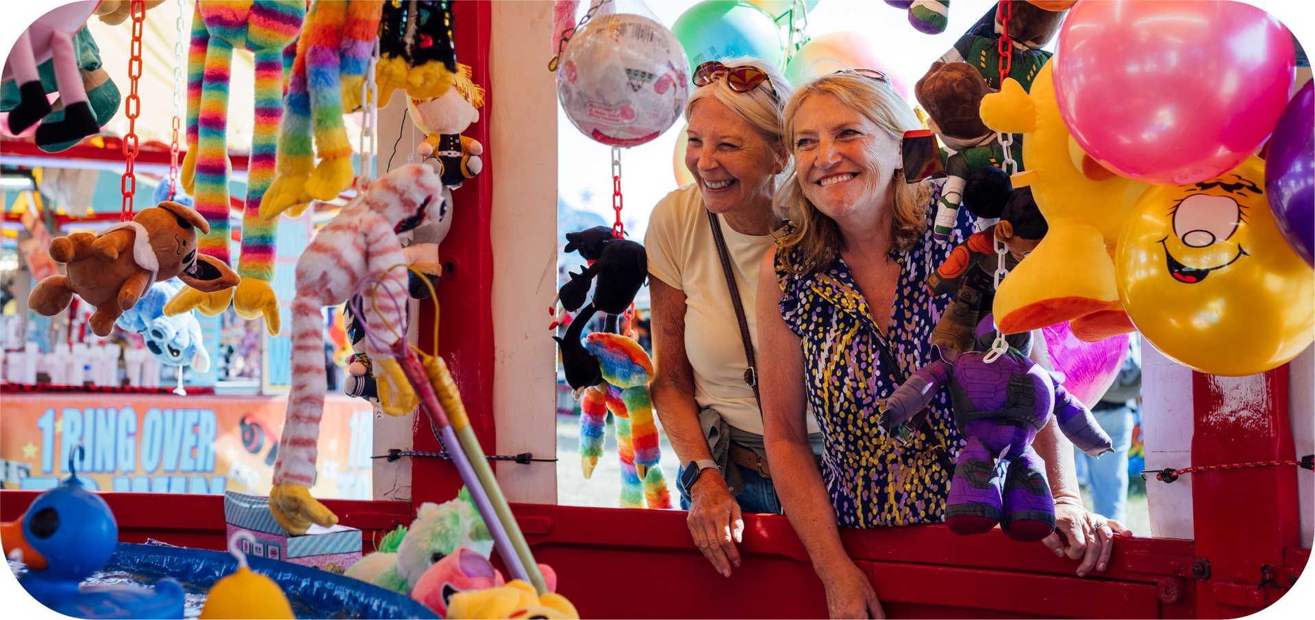 Two women are posing for a picture in a carnival booth.