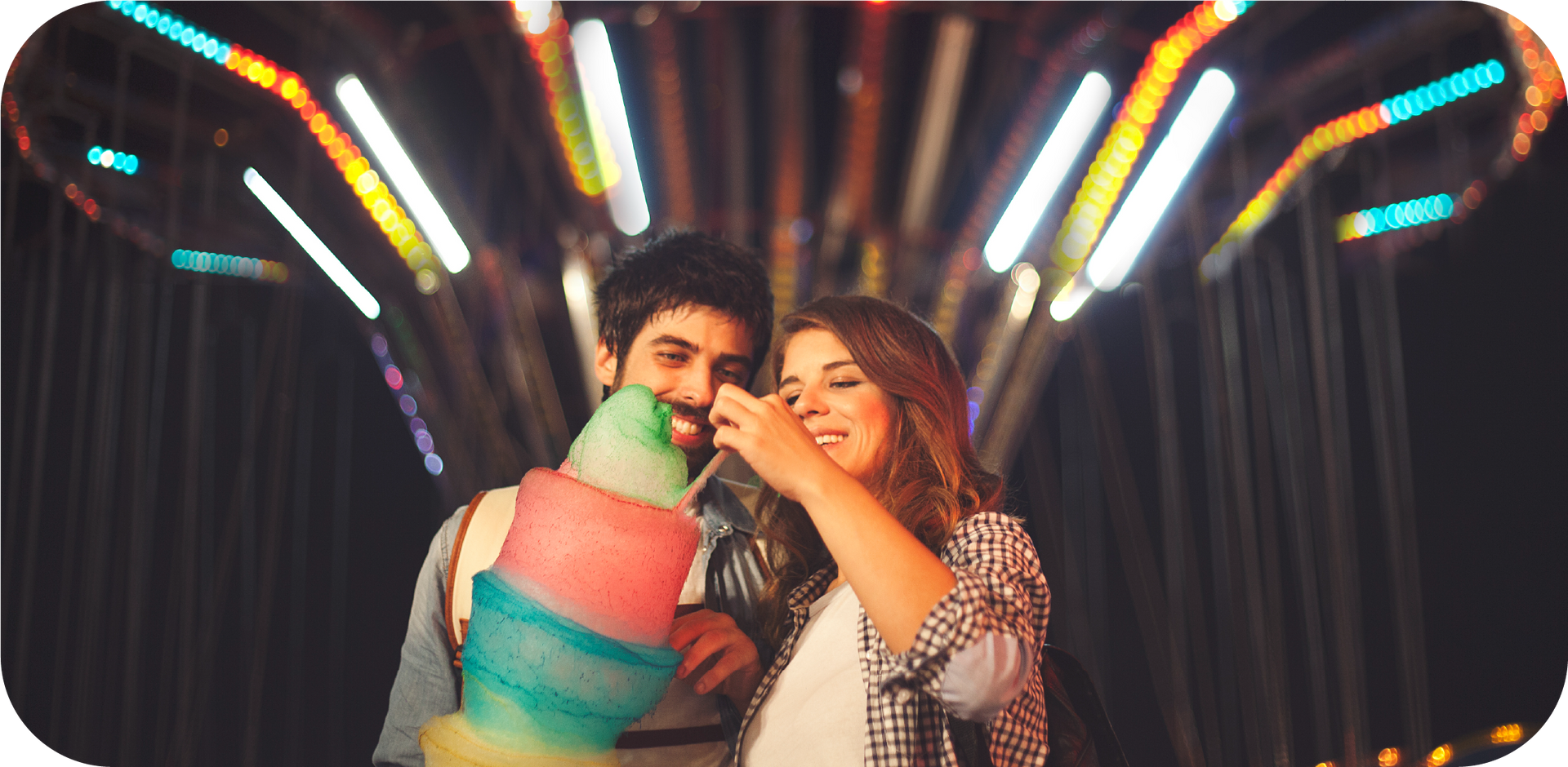 A man and a woman are eating cotton candy at a carnival.