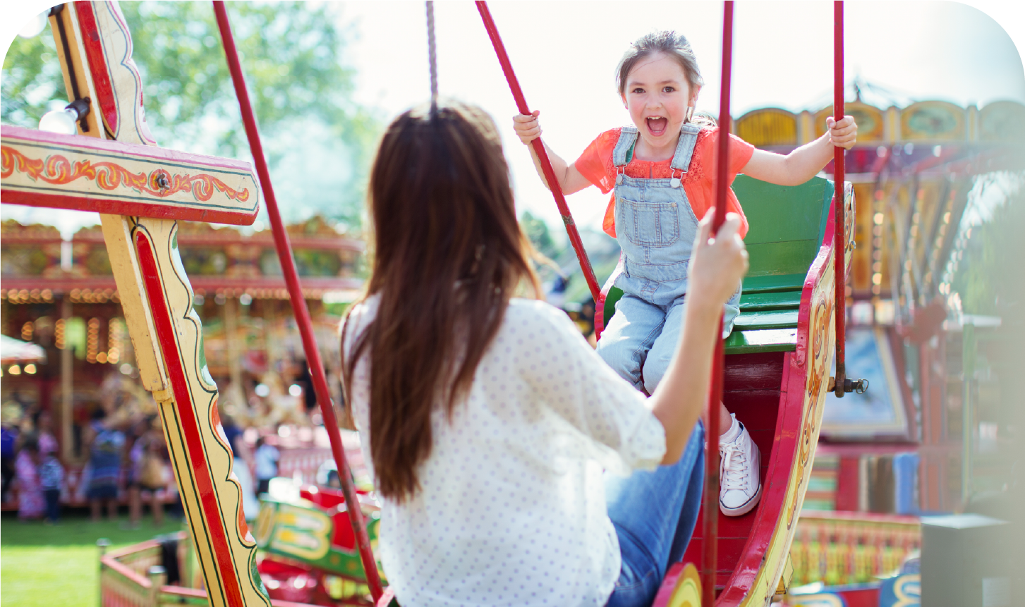 A woman is sitting on a swing with a little girl on a merry go round.