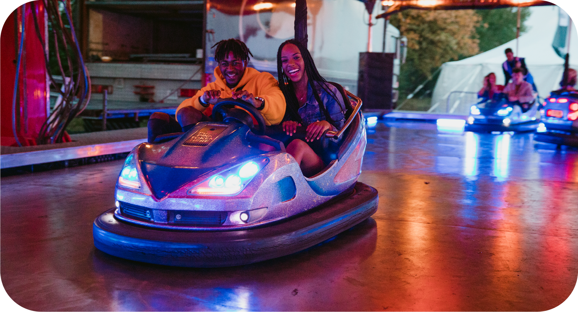 A man and a woman are riding a bumper car at an amusement park.