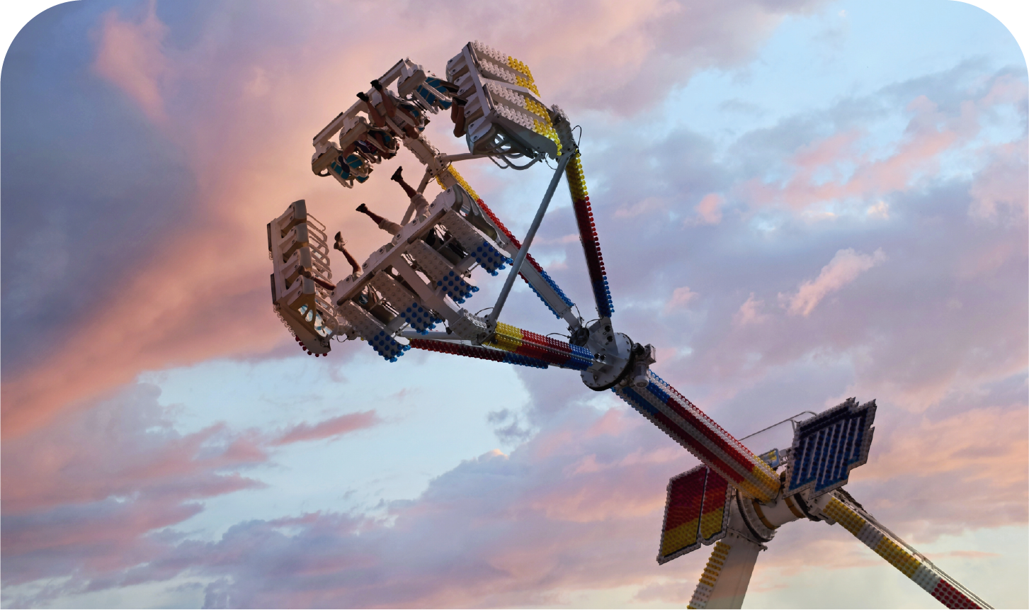 A carnival ride is flying through the air against a cloudy sky.