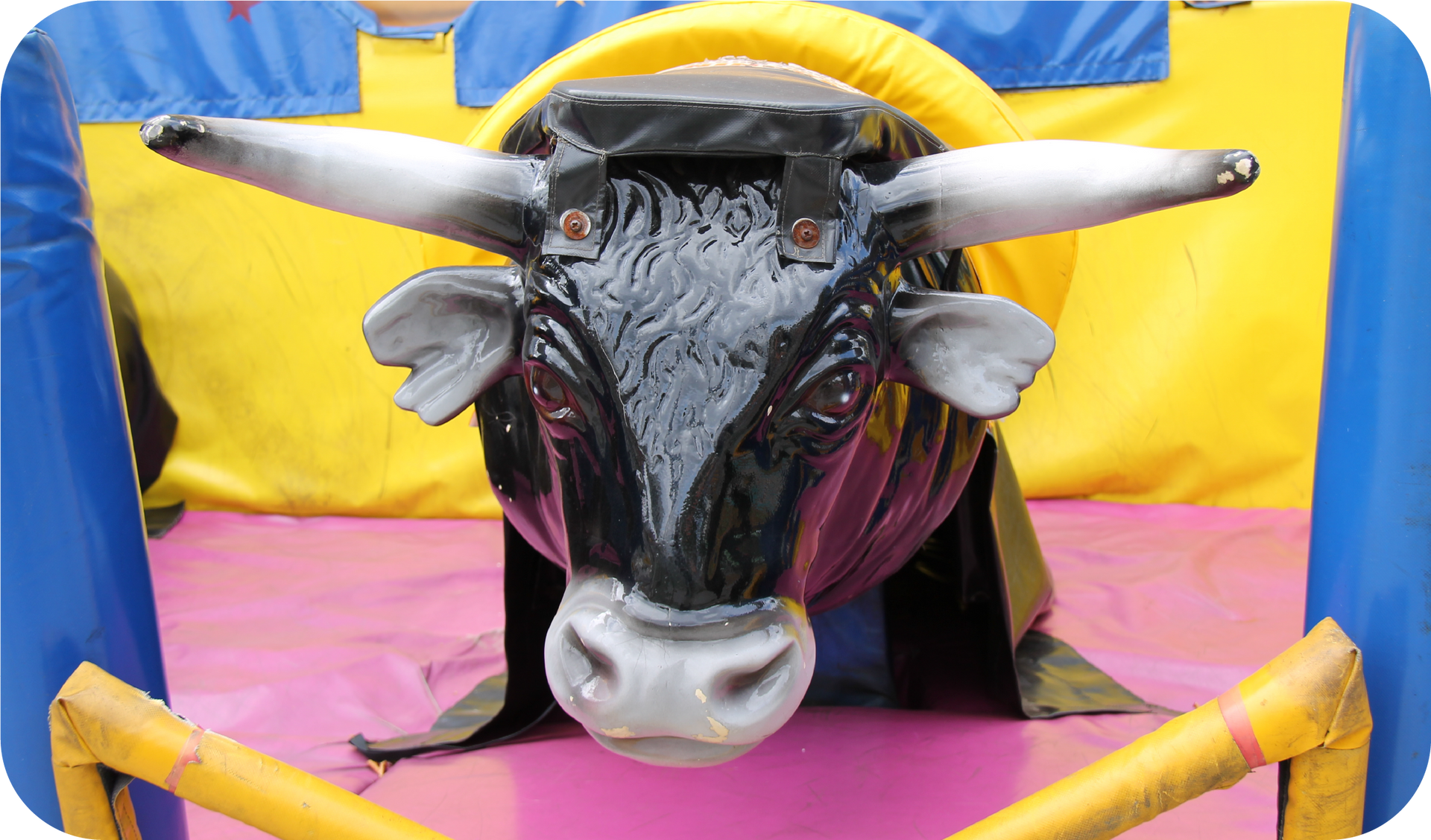 A mechanical bull is sitting in a fenced in area.