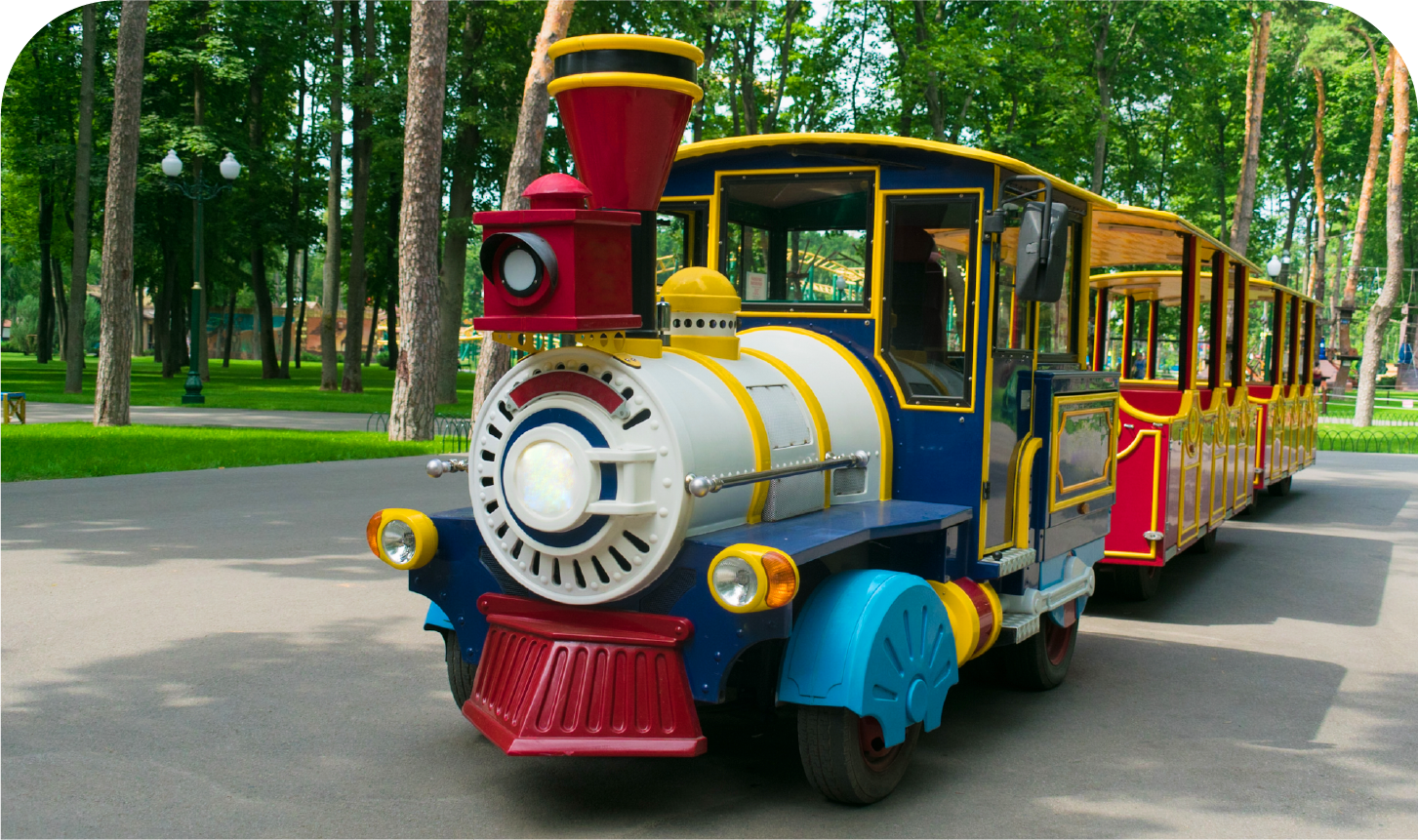 A colorful train is going down the road in a park.