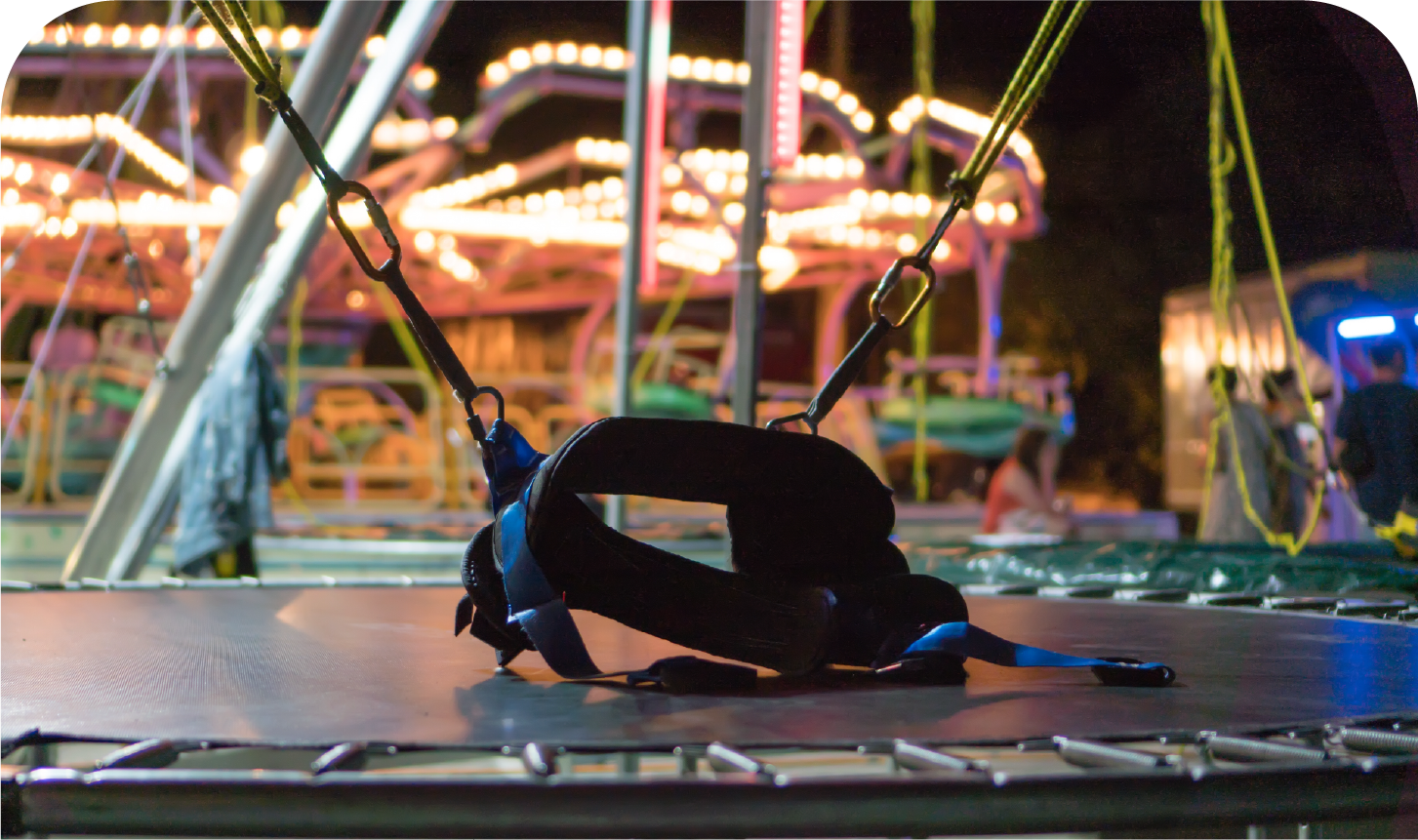 A person is laying on a trampoline at a carnival at night.