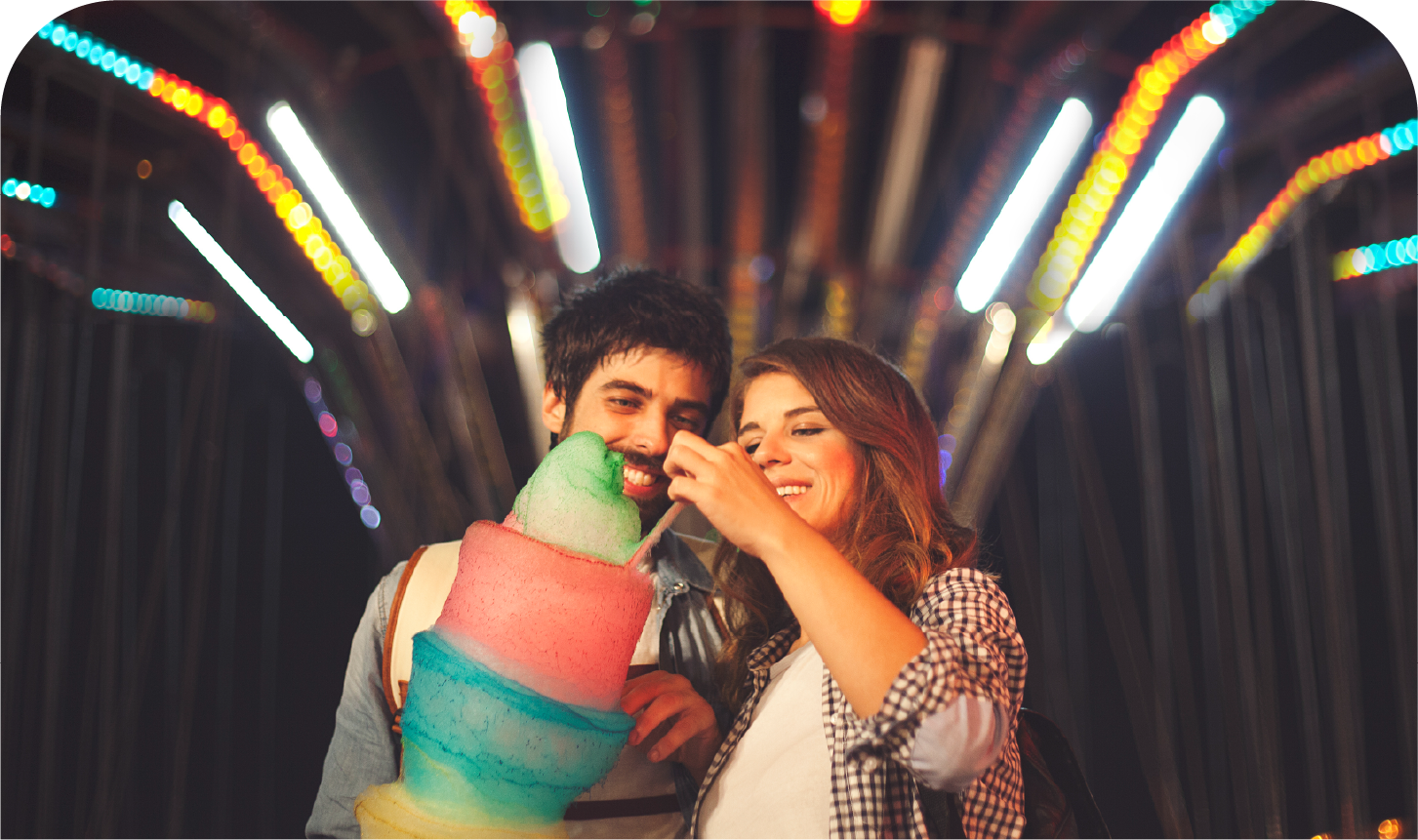 A man and a woman are eating cotton candy at a carnival.