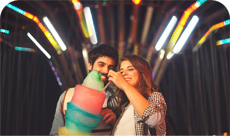 A man and a woman are eating cotton candy at a carnival.