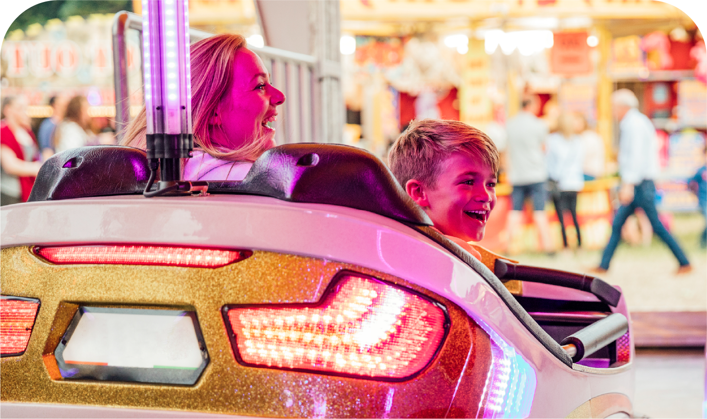 A woman and a boy are riding a roller coaster at a carnival.