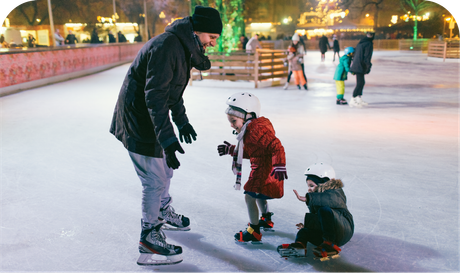 A man is helping two children ice skate on an ice rink.