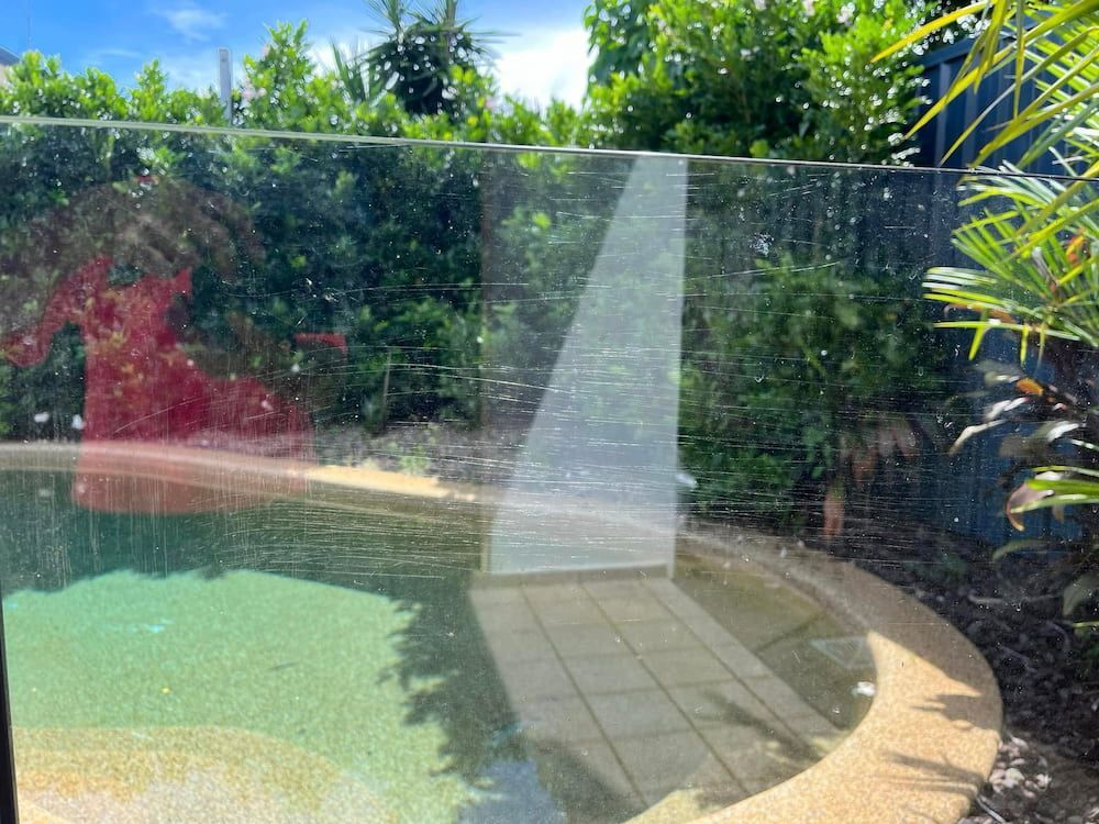 Swimming Pool With Clear Glass Barrier and Lush Green Foliage — DAH Cleaning Services In Bungalow, QLD