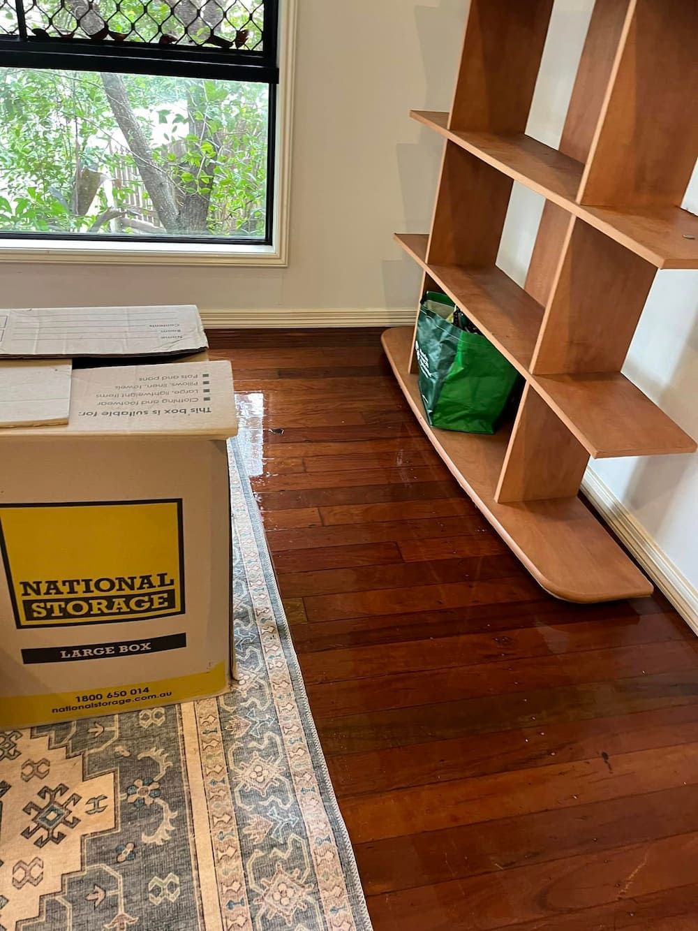 Wooden Bookshelf and Storage Box in a Room With Wood Floors and a Window — DAH Cleaning Services In Bungalow, QLD