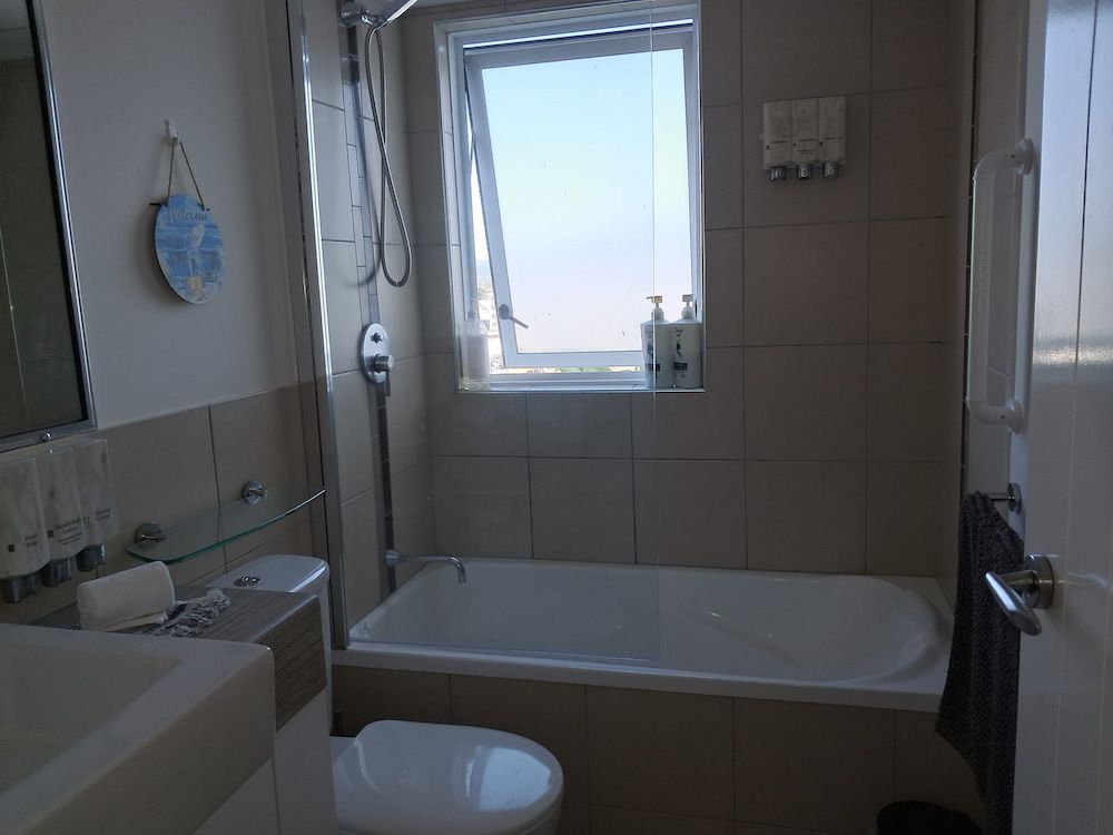 Bathroom With Tub, Toilet, and Open Window; Neutral Tiles and Light — DAH Cleaning Services In Bungalow, QLD