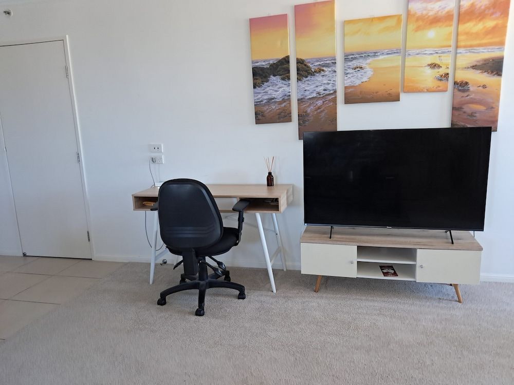 A Desk With a Black Office Chair, Tv on a Stand, and Art on the Wall in a Room — DAH Cleaning Service In Edge Hill, QLD