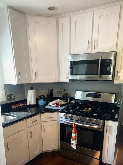 White kitchen cabinets with black countertops. Stainless steel microwave, oven/stove.