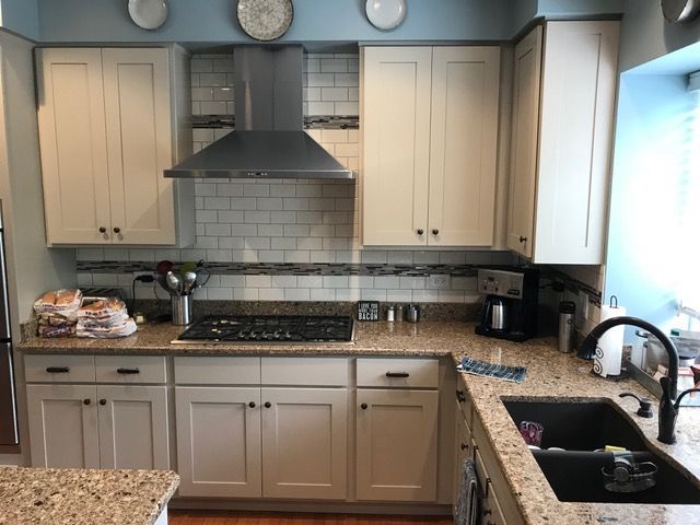 Kitchen with light cabinets, granite countertops, stainless steel range hood, and black sink.