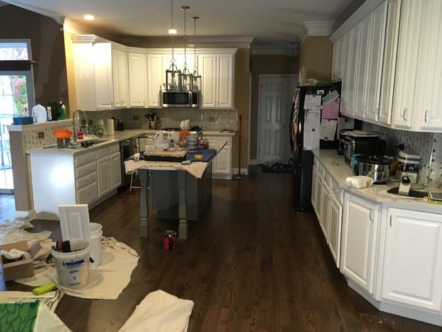Kitchen with white cabinets, dark wood floor, island, and painting supplies.
