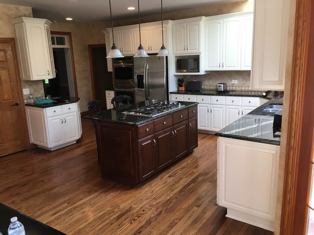 Kitchen with white cabinets, dark island, stainless steel appliances, and wood floors.