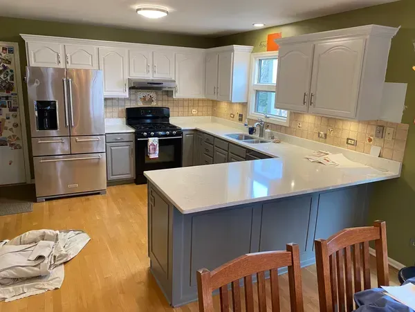 Kitchen with white and gray cabinets, stainless steel refrigerator, and light countertops.